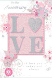 This anniversary card feels like a treasured memento discovered in a favourite Bowes Park bookshop, its design quietly glowing with affection. At the centre, the word LOVE is spelled out in raised, gently rounded letters that have been dusted with a soft, shimmering glitter. The glitter is more of a frosted gleam than a sparkle, so the letters appear almost pearlescent, inviting touch and lingering attention. The letter O subtly hints at a heart shape, adding a romantic twist without overwhelming the design. Behind and around this word stretches a tender palette of pastel pinks and soft greys, fading into pearly white at the edges, like the sky at dusk above the nearby residential streets. Clusters of delicate flowers bloom around the lettering, their petals painted in blush, mauve, and pale ivory tones. Each blossom is outlined with fine, silvery lines and gentle shading that give the illusion of depth, as though the flowers are lightly pressed onto the page, echoing the sensitivity of a florist arranging anniversary blooms with care. Curving vines, graceful swirls, and a few almost-hidden butterflies thread through the composition, adding a sense of movement and whispered joy, like a breeze passing through a garden up near Bounds Green. Elegant script phrases such as On Our Anniversary and I love you today and always are woven into the design, their flowing typography reinforcing the theme of enduring devotion. The overall impression is of a softly radiant, romantic card, perfect to accompany a bouquet delivered locally to mark a shared journey and another year of love.